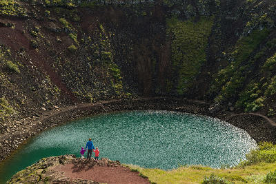 Family standing on the rim of Kerið crater above a turquoise volcanic lake in South Iceland.