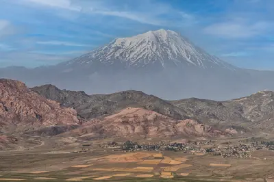 Snow-capped Mount Ararat rising behind rugged volcanic foothills and farmland in Eastern Turkey.