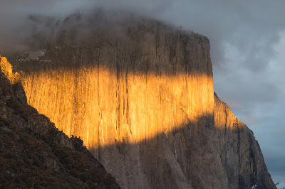 El Capitan Yosemite sunset with golden light on granite wall under dark clouds.
