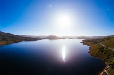 Aerial view of Lake Pedder with sunlight reflecting across the water and mountains of Southwest National Park, Tasmania.