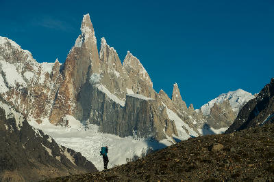 Hiker standing on a ridge with Cerro Torre peaks and glacier in the background, Patagonia, Argentina.