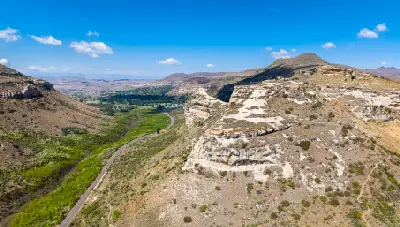Aerial view of sandstone cliffs and a winding valley road leading towards Clarens in South Africa's Eastern Highlands.