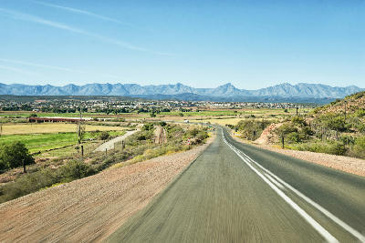 Road leading towards Oudtshoorn across the Klein Karoo valley with mountain ranges in the background, Western Cape, South Africa.