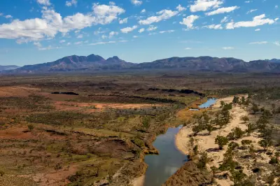A river winds through the arid landscape beneath the rugged peaks of the West MacDonnell Ranges.