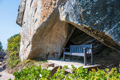 Bench beneath a large sandstone rock shelter along a hiking route in Robberg Nature Reserve, South Africa.