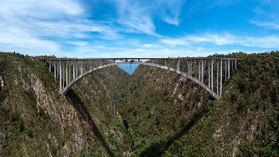 Drone view of Bloukrans Bridge crossing the steep Bloukrans River Gorge in the Tsitsikamma region of South Africa, showing the bridge arch and forested canyon walls.