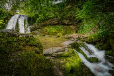 Janet's Foss waterfall and flowing stream surrounded by moss-covered rocks and green woodland near Malham, North Yorkshire, England.