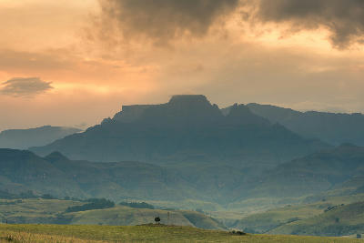 Silhouette of Champagne Castle beneath a dramatic sunset sky in the Central Drakensberg, KwaZulu-Natal, with rolling green foothills in the foreground.