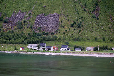 Ersfjord village Senja Norway with coastal houses along fjord shoreline beneath steep green mountain slope.
