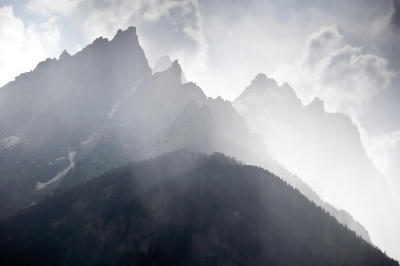 Teton Range partially obscured by cloud with sun rays illuminating the mountains, Grand Teton National Park, Wyoming, USA.
