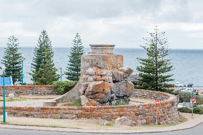Stone war memorial at The Point in Mossel Bay with ocean views and coastal pine trees along the Garden Route shoreline.