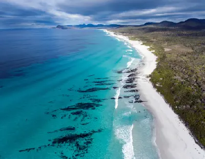 erial view of the long white-sand coastline and turquoise waters of Friendly Beaches in Freycinet National Park, Tasmania.