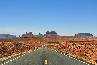 Long straight road crossing an arid desert landscape in Southern Utah with red rock mesas in the distance.