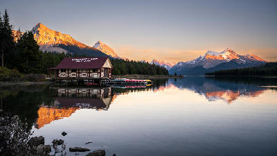 Maligne Lake boathouse at sunset with snow-capped peaks and reflections on calm water