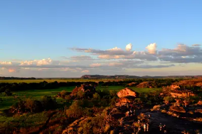 Visitors standing on sandstone outcrops at Ubirr overlooking green floodplains and distant escarpments in Kakadu National Park, Northern Territory, Australia.