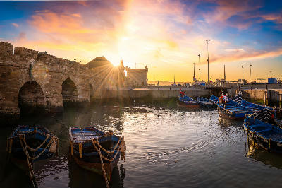 Blue fishing boats rest beneath the historic harbour ramparts of Essaouira at sunset on Morocco’s Atlantic coast.