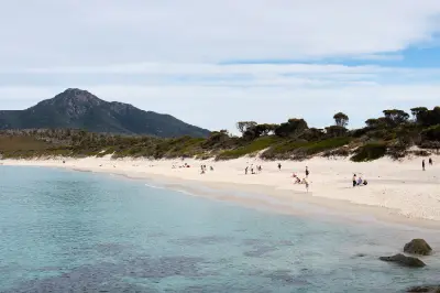 White-sand beach and turquoise water at Wineglass Bay with visitors along the shore and forested mountains rising behind, Tasmania.