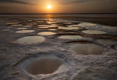 Sunset reflecting in shallow pools surrounded by white salt formations at Lake Tuz, Turkey.