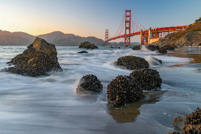 Golden Gate Bridge from Baker Beach at sunset with rocky foreground and long exposure waves