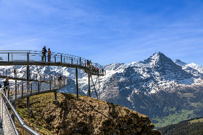 Curved First Cliff Walk platform with visitors overlooking alpine slopes and the Eiger peak in the Jungfrau region, Switzerland.