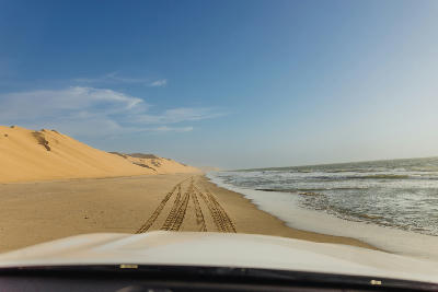 Vehicle traveling on a beach between large sand dunes and the Atlantic Ocean along Namibia’s Skeleton Coast.