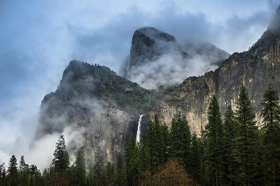 Bridalveil Fall Yosemite dropping between Cathedral Rocks with mist and low cloud around granite cliffs above pine forest.