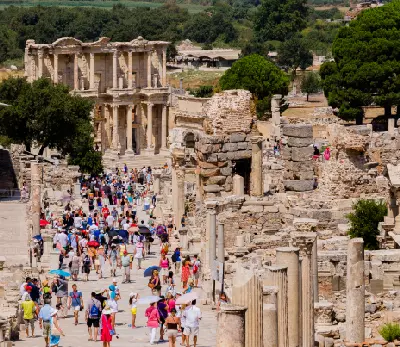 Busy Curetes Street in Ephesus filled with visitors, surrounded by ancient columns and stone ruins, with the Library of Celsus visible ahead.