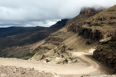Low cloud over the escarpment above Sani Pass with gravel switchbacks descending into the Drakensberg valley between Lesotho and South Africa.