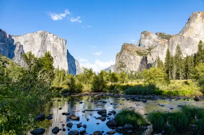 Valley View Yosemite with El Capitan and Bridalveil Fall above the Merced River with rocks and green vegetation under clear blue sky.