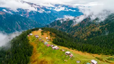 Aerial view of Pokut Plateau with scattered highland houses, dense forests and clouds drifting through the Kaçkar Mountains in Turkey.