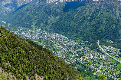 Aerial view of Chamonix town on the valley floor surrounded by steep green alpine slopes in the French Alps.