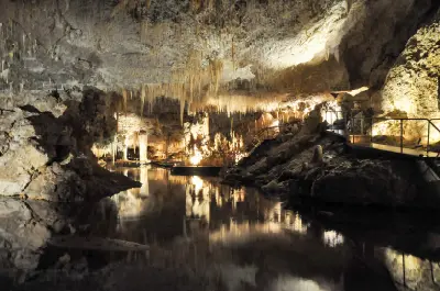 Underground lake reflecting stalactites and illuminated limestone formations inside Lake Cave, with the visitor walkway crossing the cavern.