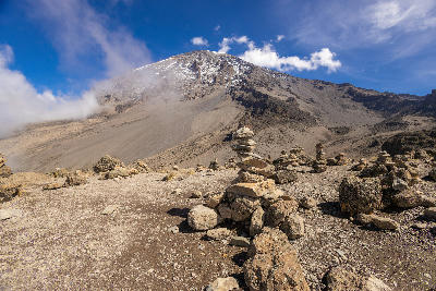 Kibo summit on Mount Kilimanjaro viewed from the upper climbing route at approximately 4,700 metres above sea level, with volcanic scree, stone cairns, and patches of snow, Tanzania.