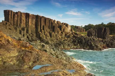 Dramatic basalt columns and rugged volcanic rock formations rise beside the ocean at Bombo Headland Quarry near Kiama, Australia.