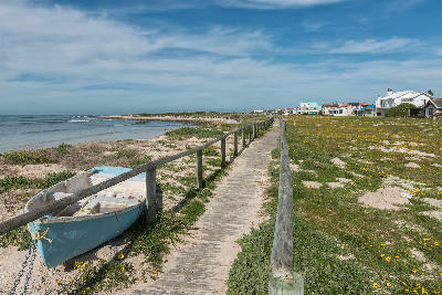 Wooden boardwalk beside the shoreline at Struisbaai with coastal homes and calm ocean views in the Western Cape.