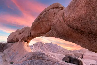 Granite rock arch with a hiker beneath it at sunset in the Spitzkoppe landscape of Namibia.