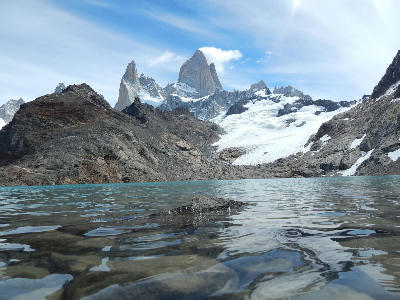 Shallow foreground water and stones at Laguna de los Tres with Mount Fitz Roy peaks rising in the background, Patagonia, Argentina.