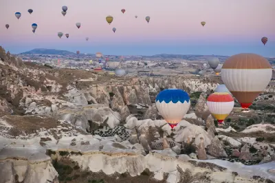 Hot air balloons floating above Rose Valley in Cappadocia, Turkey, at sunrise, with fairy chimneys, eroded rock formations, and rolling valleys stretching into the distance beneath a pastel dawn sky.