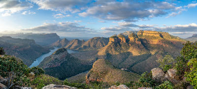 Panoramic view of the Blyde River Canyon and Three Rondavels in Mpumalanga, South Africa, with the Blyde River winding between dramatic sandstone cliffs and mountains.