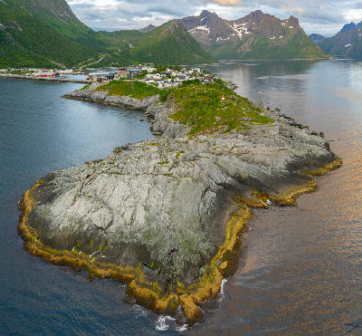 Drone view of Husøy island with compact village on rocky outcrop connected by causeway within a fjord landscape