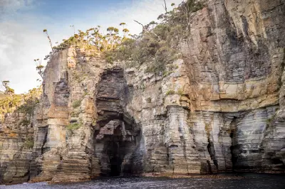 Tasman Arch and towering layered sea cliffs viewed from the water on the Tasman Peninsula, Tasmania.