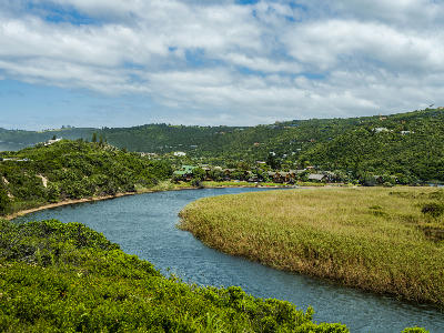 The Touw River winds through reed beds and coastal vegetation near Wilderness, with the Garden Route town and forested hills rising beyond.