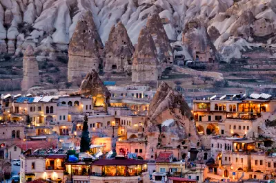 Göreme Town at dusk with illuminated cave hotels beneath towering fairy chimneys in Cappadocia, Turkey.