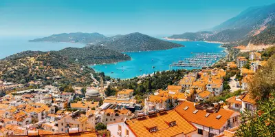 Panoramic view over Kaş, with orange-tiled rooftops, a marina filled with yachts, turquoise bays and the mountainous Mediterranean coastline.