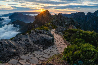 Stone path along the Pico do Arieiro–Pico Ruivo ridge at sunset, with jagged volcanic peaks and cloud-filled valleys in Madeira’s central mountains.