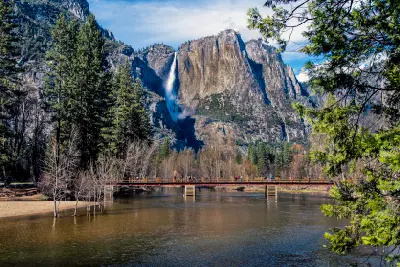 Sentinel Bridge crossing the Merced River with Yosemite Falls centered behind in Yosemite Valley.