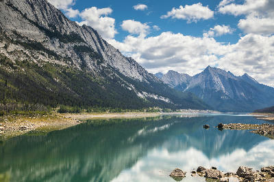 Medicine Lake reflecting mountains, clouds, and sky with calm water and rocky shoreline