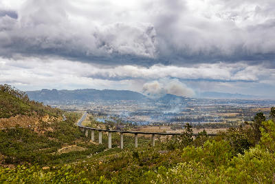 Dark storm clouds and wildfire smoke above the Paarl valley in South Africa, with the N1 bridge crossing the landscape beneath dramatic weather and hazy mountain ridges.