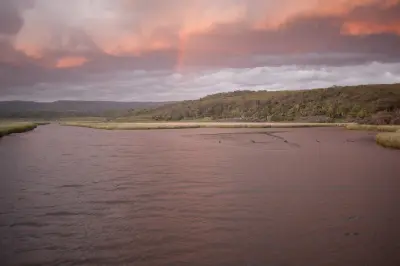 Pink sunset and faint rainbow over the Aire River estuary and surrounding forest in Great Otway National Park, Victoria.