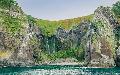 Furepe Waterfall drops in thin streams down a concave basalt cliff into the sea along the Shiretoko Peninsula.